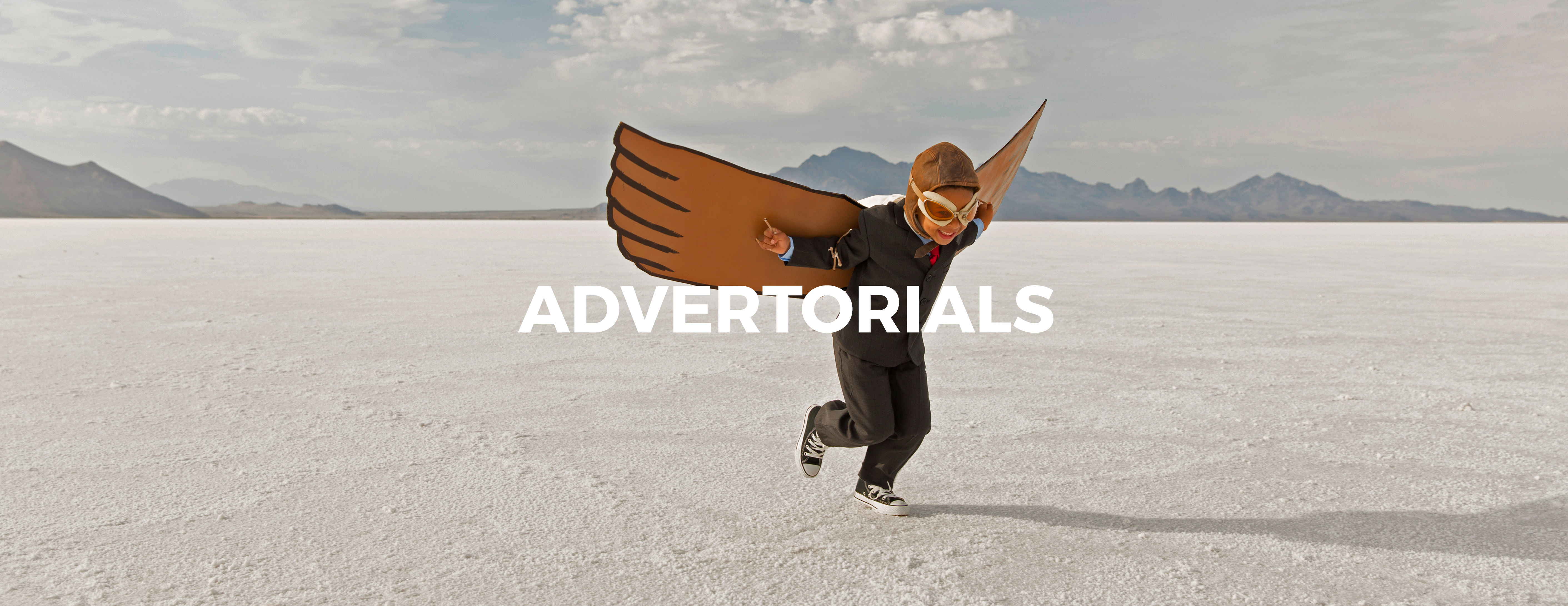 A young business boy dressed in business suit wearing cardboard wings and aviator goggles is ready to fly his business into the sky. He is running on the Bonneville Salt Flats in Utah, USA.