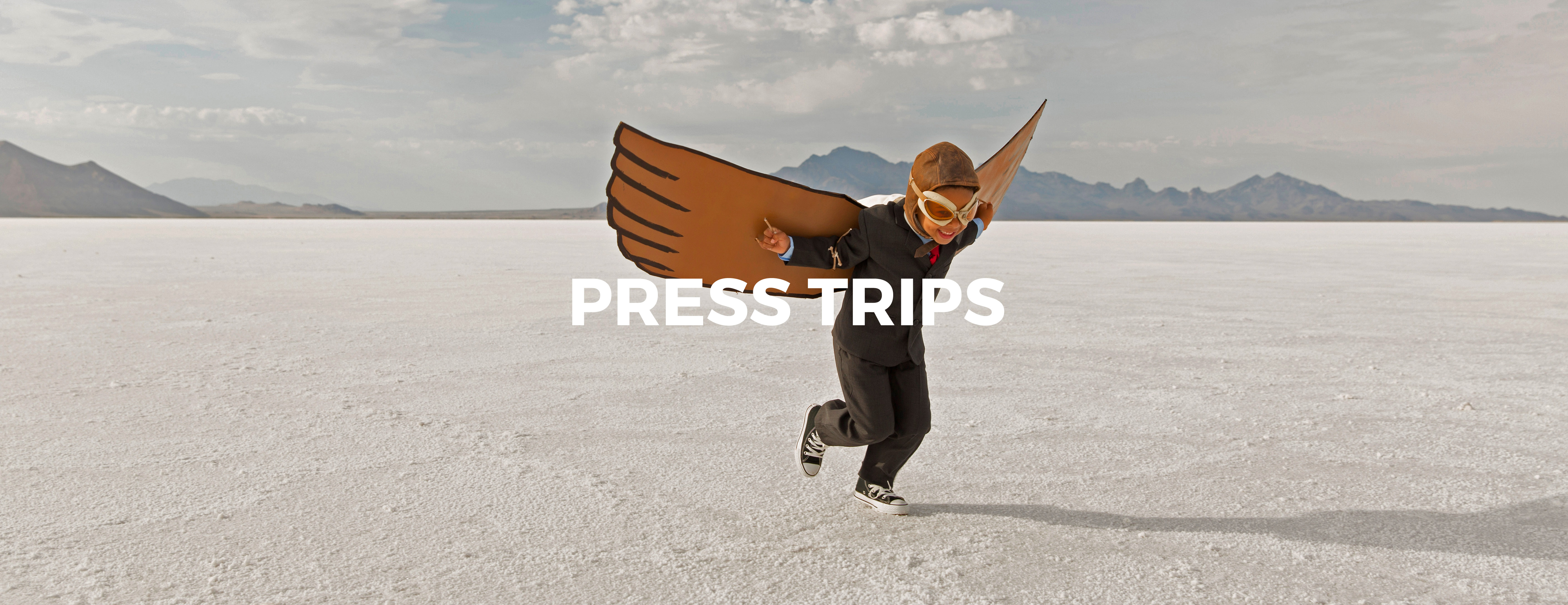 A young business boy dressed in business suit wearing cardboard wings and aviator goggles is ready to fly his business into the sky. He is running on the Bonneville Salt Flats in Utah, USA.